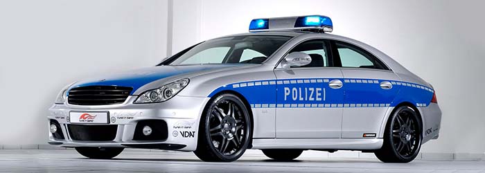 Um carro de policia Mercedez Brabus, prata e azul em uma garagem de paredes brancas.